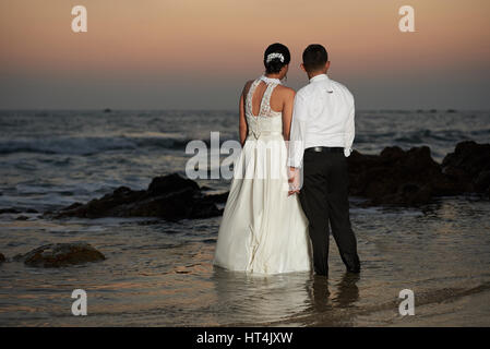 Paar Enjoing am Meeresstrand Sonnenuntergang heiratete. Braut und Bräutigam stehen am Meer Wasser Ansicht von hinten Stockfoto