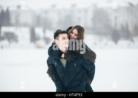 Mann trägt seine Freundin auf der Rückseite im Park, im Winterurlaub Stockfoto