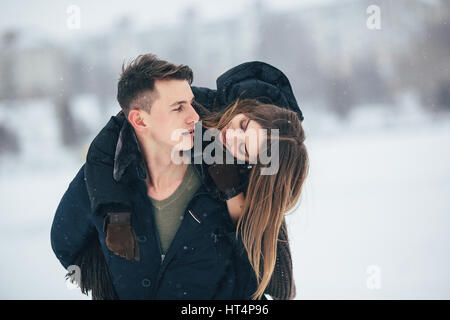 Mann trägt seine Freundin auf der Rückseite im Park, im Winterurlaub Stockfoto