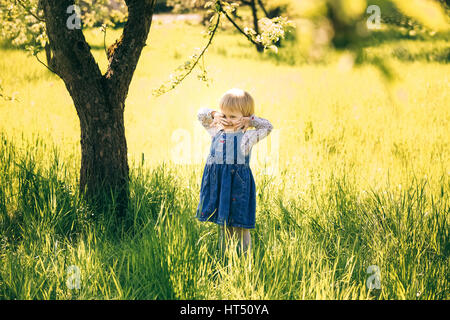 Porträt von glückliches Kind stehend unter riesigen alten Apfelbaum im Frühlingsblüten. Kleine Mädchen spielen fröhlich im Garten Landschaft. Alter des Kindes 2 Stockfoto