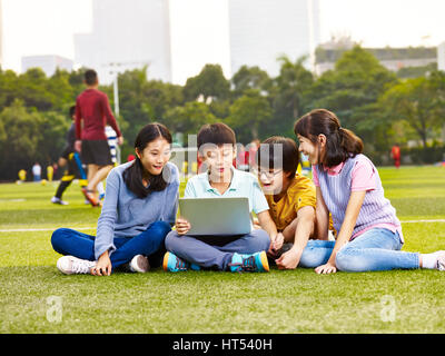 Gruppe von asiatischen Grundschülern sitzen auf Spielplatz Rasen Blick auf Laptop-computer Stockfoto