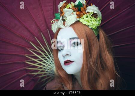 Frau, gekleidet wie eine Geisha-Mädchen mit Sonnenschirm und Blumengirlande im Haar Stockfoto