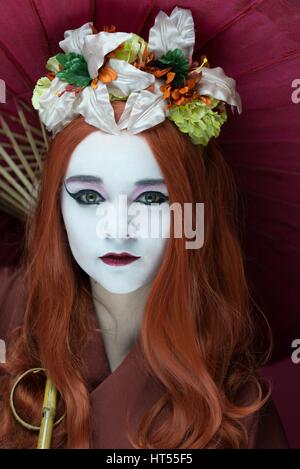 Frau, gekleidet wie eine Geisha-Mädchen mit Sonnenschirm und Blumengirlande im Haar Stockfoto