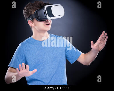 Erstaunt teenboy tragen virtual-Reality Brille Filme oder Videospiele spielen, auf schwarz. Überrascht Teenager auf der Suche in VR-Brille. Emotionale Stockfoto