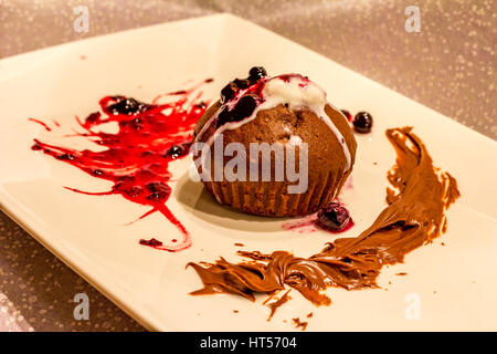 Platte von Muffin mit einem Zweig rote Johannisbeere Eis mit roter Marmelade und Minze bestreut mit Puderzucker. Schokolade Kuchen mit Eis, Beeren und Minze. Stockfoto