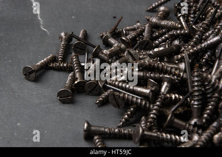 Techno-Hintergründe - schwarz geölt Haufen Schrauben auf einem dunklen grauen Karton Stockfoto