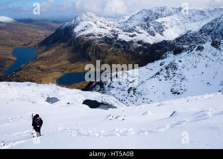 Wanderer, Wandern im Schnee auf Y Garn Bergrücken mit Blick auf Ogwen Valley und Glyderau Berge in Snowdonia-Nationalpark. Ogwen, Gwynedd, Nordwales, UK Stockfoto