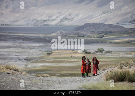 Afghanistan, Wakhan-Korridor, drei Mädchen in bunten Trachten zu Fuß durch das Tal zwischen den Bergen. Stockfoto