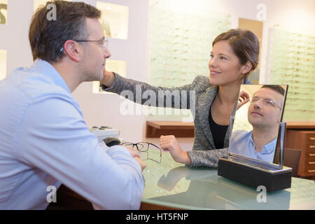 hübsche Verkäufer helfen, die Wahl Brillen in Optiker Stockfoto