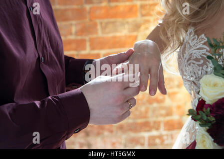 Hände hautnah, wenn der Bräutigam den Ring der Braut bei der Trauung vor dem Fenster platziert Stockfoto