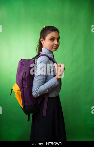 ein Teen Schulmädchen im blauen Hemd ist mit einem lila Rucksack auf den Schultern auf einem grünen Chroma Key Hintergrund stehend Stockfoto