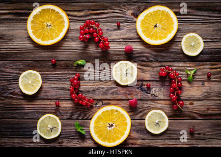 Zitrone und orange Ringe, rote Johannisbeeren, Himbeeren und Minze Blätter auf hölzernen Hintergrund. Ansicht von Tabelle oben. Frisches Obst Zusammensetzung / Layout. Stockfoto