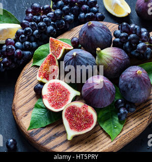 Frische schwarze Trauben, Zitronen und lila Feigen auf Holzbrett mit Wasser besprüht. Stillleben mit frischen Früchten. Quadratische Ernte Stockfoto