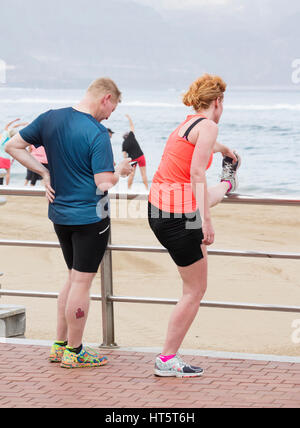 Jogger, die Dehnung mit Blick auf Strand. Mann am Handy-Bildschirm Stockfoto