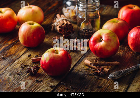 Rote Äpfel mit verschiedenen weihnachtlichen Gewürzen auf Holztisch. Stockfoto