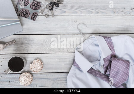 Fragment von einem Herren Hemd mit Krawatte auf einen Kleiderbügel, Cracker, Kaffeetasse auf einer lackierten Holzoberfläche. Pastell-Farben Stockfoto