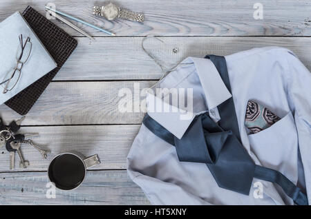 Fragment einer Herren Hemd mit Krawatte auf einen Kleiderbügel, Tagebuch, Kaffeetasse auf einer lackierten Holzoberfläche. Pastell-Farben Stockfoto