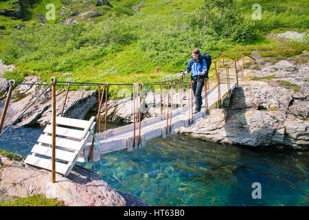 Junge Frau mit Rucksack wandern über schmale hölzerne Hängebrücke über den kleinen Fluss Stockfoto