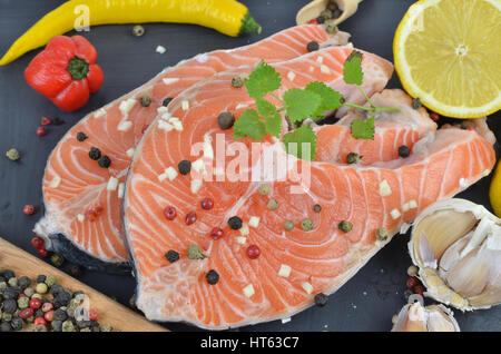 Frischer Lachs Steaks auf schwarze Holzoberfläche umgeben mit Gewürzen Stockfoto