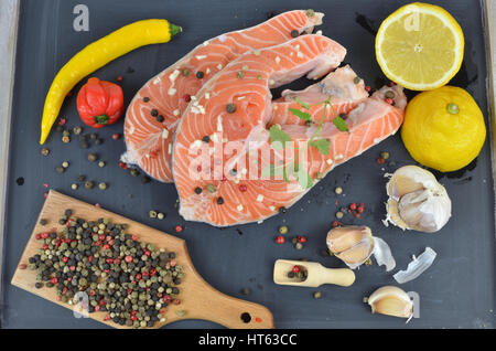 Frischer Lachs Steaks auf schwarze Holzoberfläche umgeben mit Gewürzen, Zitrone und Knoblauch Stockfoto