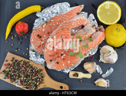 Saftige Lachs Steaks auf schwarze Holzoberfläche umgeben mit Gewürzen, bereit für grill Stockfoto