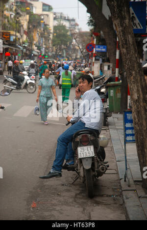 Mann sitzt auf seinem Motorrad, während er telefoniert, Hanoi, Vietnam. Stockfoto