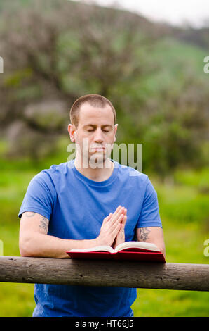 Mann, der betet allein außen mit Hände zusammen auf ein offenes Buch. Stockfoto