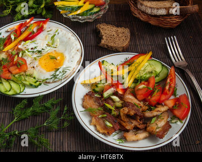 Gebratener Speck, Eiern und Gemüse mit Paprika, Tomaten und grünen auf weißen Platten auf einem Tisch auf einem Bambus-Serviette Stockfoto