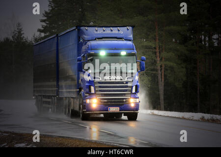 SALO, Finnland - 4. März 2017: Blaue Scania R620 Kombination Fahrzeug von M. Keskimaki Transporte waren auf nasser Fahrbahn bei Schneefall, blitzte Fernlicht br Stockfoto