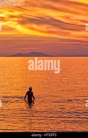 Silhouette von ein paar Schwimmen im Meer vor dem Hintergrund der den Sonnenuntergang an einem Strand mit schönen dramatischen orange und rote Himmel. Stockfoto