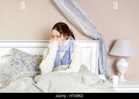 Grippe. Nahaufnahme Bild des frustrierten kranke Frau im Bett liegend in dicken blauen Schal hält Gewebe durch ihre Nase. Stockfoto