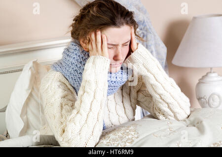 Grippe oder Erkältung. Closeup Draufsicht Bild der frustrierte junge Frau mit blauen Schal und Leiden schreckliche Kopfschmerzen beim liegen im Bett. Stockfoto