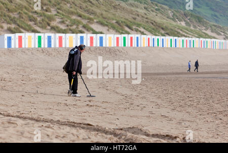 Woolacombe, Vereinigtes Königreich - 18. Mai 2011: Mann nutzt einen Metalldetektor auf Woolacombe Strand, mit bunten Strandhäuschen und 2 weiteren Personen heraus-von- Stockfoto