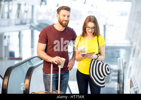 Junge Brautpaar aufstehen mit Gepäck auf der Rolltreppe zum Abflugbereich des Flughafens während ihrer Sommerferien Stockfoto