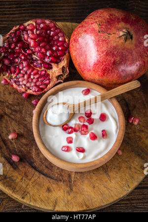 Joghurt mit Granatäpfeln in Holzschale auf rustikalen Tisch. Ansicht von oben. Stockfoto