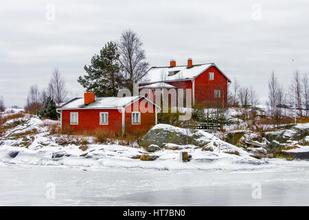 Rotes Holzhaus auf einer Insel von Wasser umgeben und bedeckt in Schnee und Eis im Winter in Helsinki, Finnland. Stockfoto