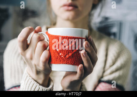Junge Frau in Pullover heißen Kaffee in roter gestrickter Handschuh aus Becher trinken. Gebündelt, bekommen Sie warme Konzept Stockfoto