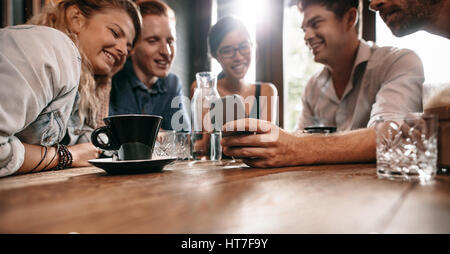 Horizontalen Schuss von jungen Freunden Fotos auf dem Handy anschauen. Gruppe von jungen Leuten am Café-Tisch sitzen und mit Blick auf Smartphone. Stockfoto