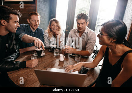 Gruppe junger Freunde mit Laptop im Café sitzen und diskutieren. Junge Männer und Frauen auf der Suche am Laptop im Café. Stockfoto