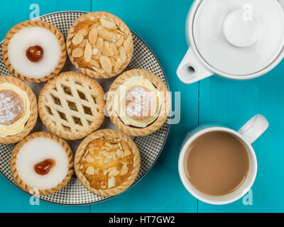 Teller mit sortierten individuelle Torten oder Törtchen mit einer Kanne Tee auf blauem Grund Stockfoto