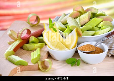 Geschälten und gehackten rohen Rhabarber Kompott mit braunem Zucker und Zitrone, im Hintergrund andere Rhabarber Kochen vorbereitet Stiele in soft-Fokus Stockfoto