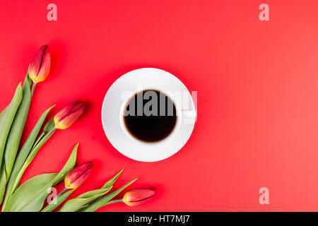 Tulpen und Tasse Kaffee auf rotem Grund. Ansicht von oben Stockfoto