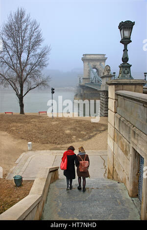 Damen, die neben der Donau und Széchenyi Kettenbrücke halb verborgen im Nebel zu wandern. Budapest, Ungarn. Foto von der Seite von Pest. Stockfoto