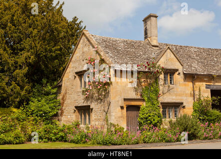 Altes Landhaus aus Stein mit rosa, rote Rosen, Efeu klettern die Wand, in der englischen Landschaft Dorf, an einem sonnigen Sommertag. Stockfoto