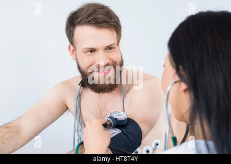 Glücklich männlichen Patienten betrachten Ärztin überprüfen Blutdruck im Krankenhaus Stockfoto