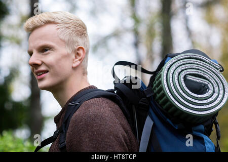 Seitenansicht der junge Mann mit Rucksack und gerollte Matte, Wandern im Wald Stockfoto