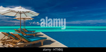Liegestühle mit Sonnenschirmen am exotischen Resort auf den Malediven mit Infinity-Pool und Strand Stockfoto