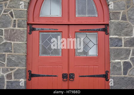 Rote Kirche Holztür mit Glasfenstern auf Metall Scharniere in Steinmauer. Stockfoto