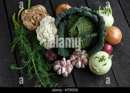 Frühling Gemüse auf einem dunklen Hintergrund: Wirsing, Blumenkohl, Zwiebeln, Knoblauch, Kohlrabi, Sellerie, Dill. Ansicht von oben. Lay-flat Stockfoto