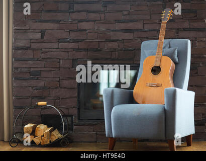 Gemütliches Wohnzimmer mit Gitarre auf dem Sessel vor dem Kamin Stockfoto